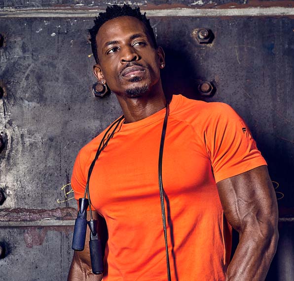 Teagan posing with gym equipment wearing an orange t-shirt